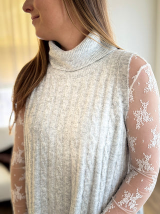 Woman wearing a light gray sweater with sheer sleeves featuring floral lace details.
