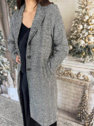 Person wearing a long, patterned coat in front of a decorated Christmas tree.