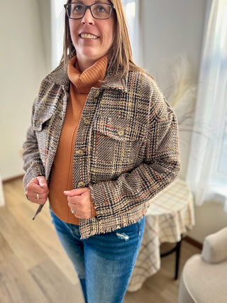 Woman wearing a patterned jacket over a brown sweater and blue jeans in a room.