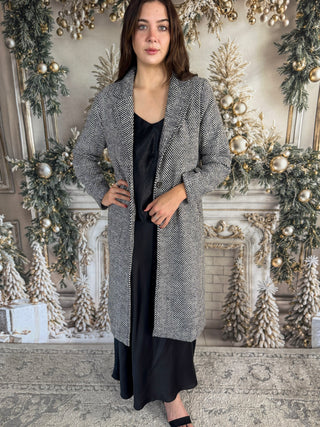 Woman wearing a long, patterned coat standing in a decorated room with Christmas trees and ornaments.