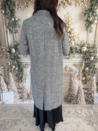 Person wearing a long, patterned coat in a decorated room with Christmas trees and lights.