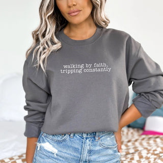 Person wearing a gray sweatshirt with text, standing against a neutral background