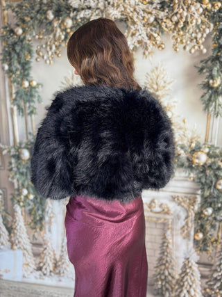 Person wearing a black fur coat in front of a decorated Christmas fireplace.