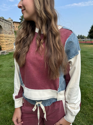 A woman wearing a color-blocked patchwork sweatshirt and matching sweatpants in an outdoor grassy park setting.