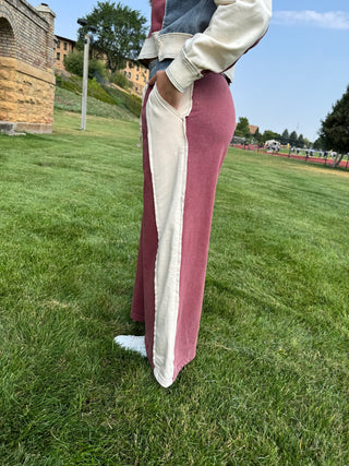 A person standing on a grassy lawn wearing a long-sleeve maxi dress with a dusty rose and cream color-blocked design, paired with a denim jacket and white sneakers.