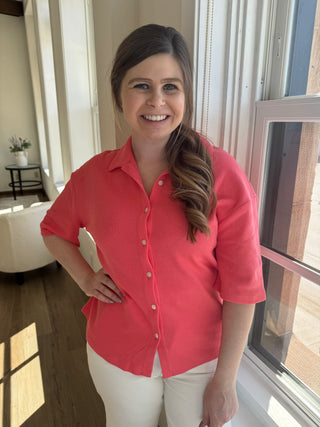 Lady standing by window wearing coral waffle knit button up boulse.