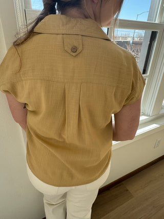 Photo of a woman in a tan button up top with two front pockets.