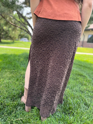 A person standing outdoors on grass wearing a dark brown textured midi skirt with a side slit and an orange sleeveless top.