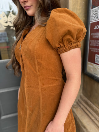 A woman wearing a rust-orange corduroy dress with puffed short sleeves and a front zipper, shown in a close-up outdoor shot.