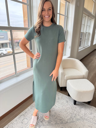 A person wearing a sage green maxi dress with a round neckline, short sleeves, and side slits.