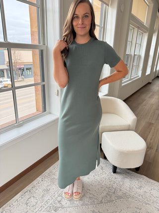 A person wearing a sage green maxi dress with a round neckline, short sleeves, and side slits.