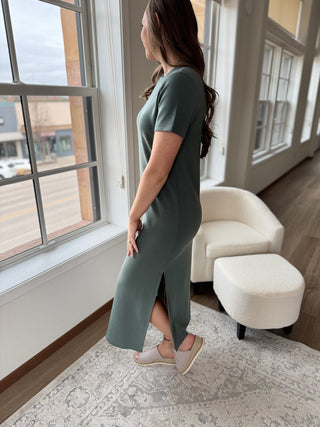 A person wearing a sage green maxi dress with a round neckline, short sleeves, and side slits.
