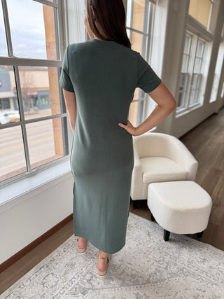 A person wearing a sage green maxi dress with a round neckline, short sleeves, and side slits.