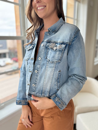 Photo of a woman smiling, wearing a denim jacket over an orange jumpsuit.
