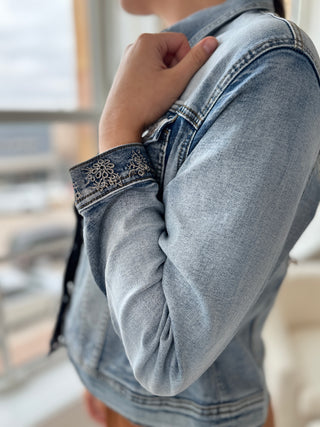 Photo of a woman smiling, wearing a denim jacket over an orange jumpsuit.