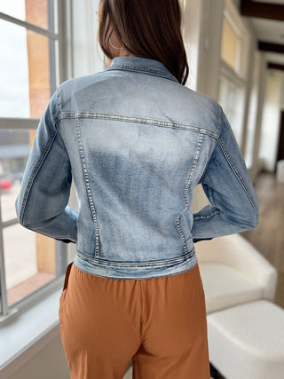 Photo of a woman smiling, wearing a denim jacket over an orange jumpsuit.