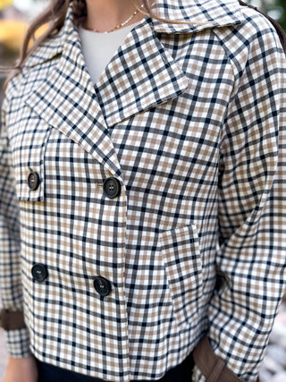 A close-up of a person wearing a cropped double-breasted plaid jacket with a tan, white, and navy gingham pattern, featuring dark buttons and a pointed collar.