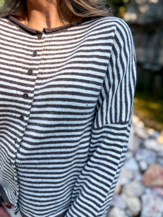 A close-up of a person wearing a fuzzy long-sleeve henley top with horizontal black and white stripes, featuring a dark brown ribbed crew neck and button closure.
