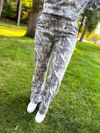 Gray and white camouflage fleece sweatpants worn by a person standing on a green grassy lawn outdoors.