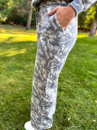 Gray and white camouflage patterned sweatpants worn by a person standing on a green grass lawn.