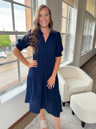 Photo of a woman wearing a long navy dress with ruffles.