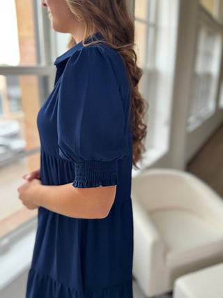 Woman wearing a blue dress standing by a window