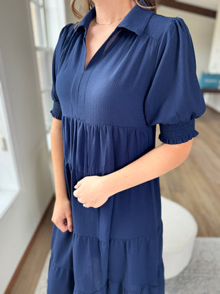 Photo of a woman wearing a long navy dress with ruffles.
