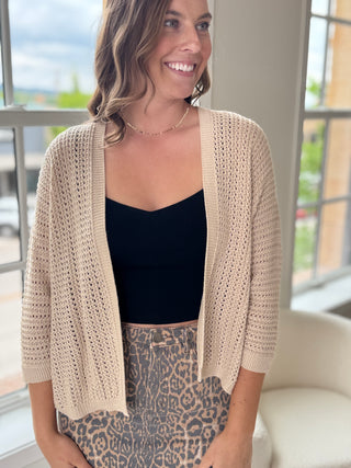 Woman wearing a beige cardigan over a black top and leopard print skirt indoors.