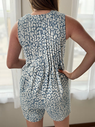 Person wearing a blue and white patterned romper in a bright room with sheer curtains.