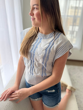 Woman wearing a patterned sweater and denim shorts indoors.