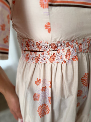 Close-up of a beige dress with orange floral patterns on a plain background