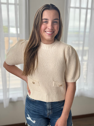 Woman wearing a beige knitted sweater and blue jeans indoors with light background