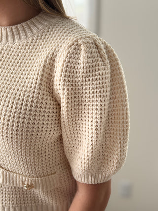 Close-up of a beige knitted sweater with puff sleeves on a neutral background