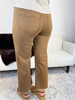 A person shown from the back wearing tan straight-leg jeans with back patch pockets, paired with a cream ribbed sweater and brown espadrille sandals in a living room setting.