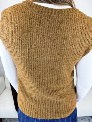 A person shown from the back wearing a sleeveless, ribbed knit sweater vest in a warm camel brown color over a white long-sleeve shirt and blue pinstriped pants.