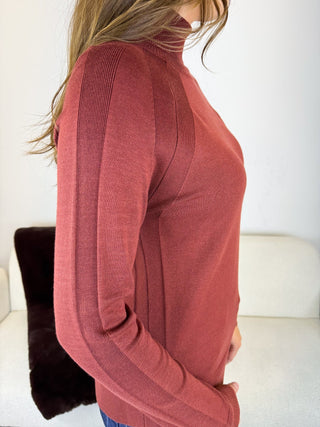 A woman wearing a ribbed long-sleeve mock neck sweater in a dusty rose color, shown from a side profile view.