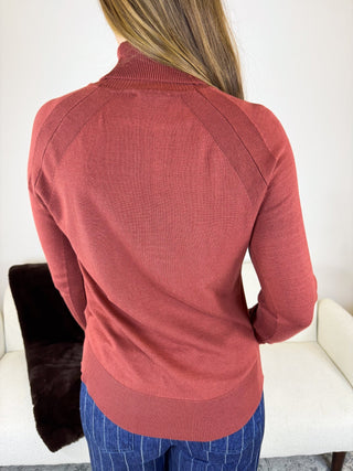 A woman viewed from behind wearing a ribbed long-sleeve mock neck sweater in a dusty rose color, paired with blue pinstriped pants, in an indoor setting.