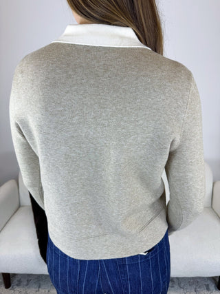 A person shown from the back wearing a light heather gray knit sweater with a contrasting white collar, paired with blue pinstriped pants, in front of a light gray sofa.
