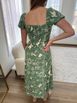 Person wearing a green dress with white floral pattern in a room.