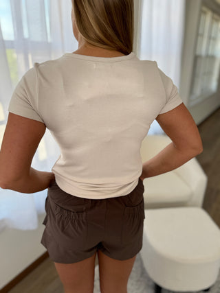 Person wearing a beige t-shirt and brown shorts standing indoors.