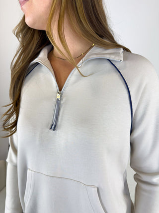 A close-up of a woman wearing a light gray quarter-zip pullover sweatshirt with dark navy piping along the shoulders and collar.