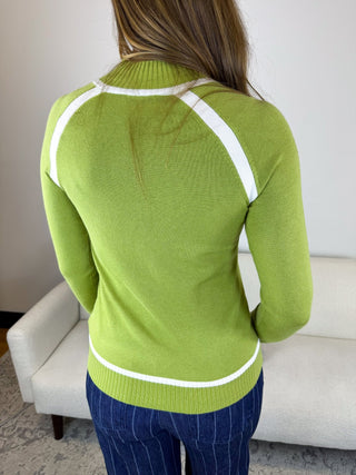 A woman viewed from behind wearing a lime green ribbed knit sweater with contrasting white trim along the collar, shoulders, and hem, paired with dark blue pinstriped pants in an indoor setting.