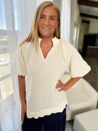 Woman wearing a white blouse with a subtle pattern in a bright room.
