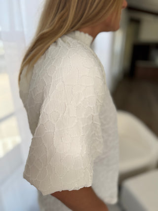 Person wearing a white lace top with a blurred background
