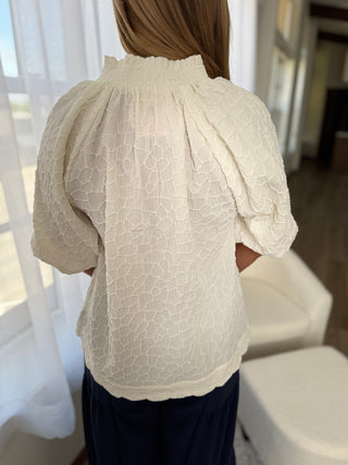 Person wearing a beige blouse with intricate patterns in a softly blurred indoor setting