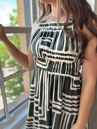 Woman wearing a black and white patterned dress standing by a window.