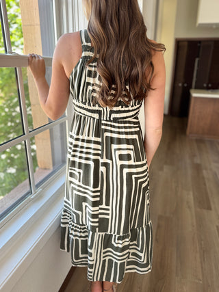 Woman wearing a black and white patterned dress standing by a window.