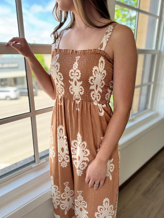 Woman wearing a brown dress with white lace patterns in a bright room.