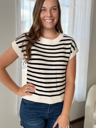 Woman wearing a black and white striped sweater with blue jeans indoors.