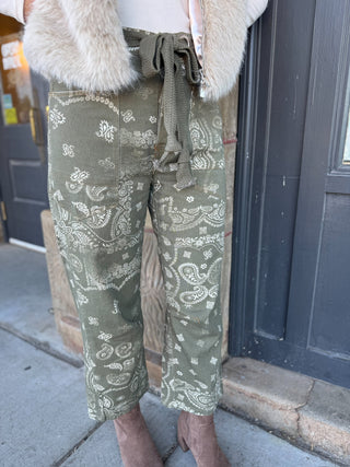 Olive green cropped pants with a white paisley bandana print, styled with a beige faux-fur vest and brown boots on a sidewalk.